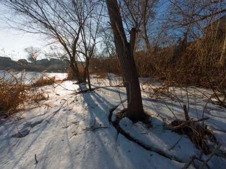 Eis auf dem Fluss. Spaziergang auf dem zugefrorenen Fluss. Ein Mann geht auf Schnee und Eis. Gefährliches Eis. Eiswasser. Tiefe Risse im Eis. Wintersonnige Landschaft mit einem Fluss. Winter Fluss und Sonne.