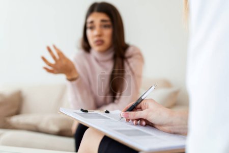 Foto de Mujer en sesión de terapia. Psicólogo atento. Psicóloga atenta sosteniendo lápiz en sus manos haciendo notas escritas mientras escucha a su cliente - Imagen libre de derechos