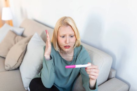 Triste, inquiète femme vérifiant son récent test de grossesse, assis sur le canapé à la maison. Maternité, accouchement et problèmes familiaux concept. grossesse non désirée