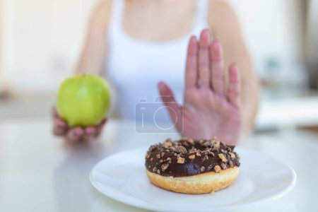 Foto de Dieta o buen concepto de salud. Mujer joven rechazando comida chatarra o comida poco saludable como donut o postre y eligiendo comida saludable como fruta o verdura fresca
. - Imagen libre de derechos