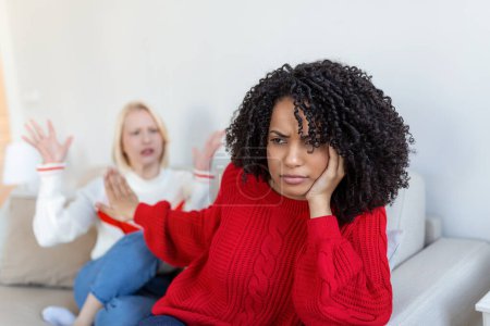 Photo for Dont want to hear. Unhappy disturbed tired woman communicating with her friend sitting near her on the sofa shaking her hands. Friends arguing on sofa at home. Two female friends arguing - Royalty Free Image