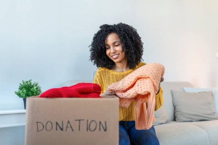 Photo for Woman holding cardboard donation box full with clothes. Concept of volunteering work, donation and clothes recycling. Helping poor people - Royalty Free Image