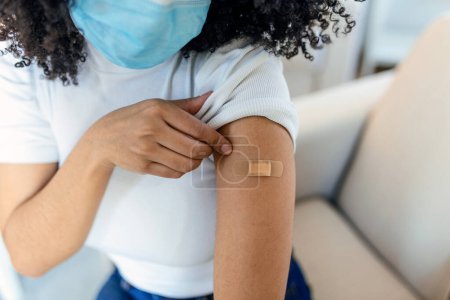 Photo for African woman holding up her shirt sleeve and showing her arm with bandage after receiving vaccination. covid 19 immunization - Royalty Free Image