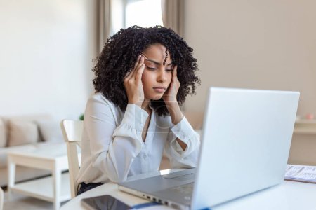 Photo for Young frustrated woman working at office desk in front of laptop suffering from chronic daily headaches, treatment online, appointing to a medical consultation, electromagnetic radiation, sick pay - Royalty Free Image
