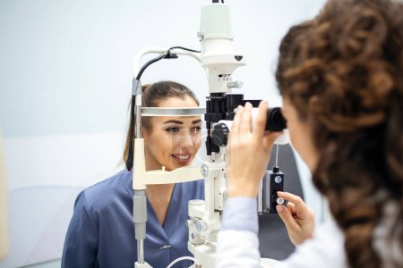 Foto de La oftalmóloga doctora está revisando la visión ocular de una joven atractiva en una clínica moderna. Médico y paciente en clínica oftalmológica - Imagen libre de derechos