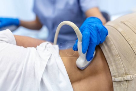 joven doctora examinando riñón de paciente con ecografía. Foto de cerca de la parte inferior de la espalda de una mujer joven que se hace una prueba de ultrasonido en la clínica. Mano de un médico que sostiene el escáner de ultrasonido.