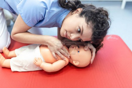 Photo for CPR practitioner examining airway passages on infant dummy. Model dummy lays on table and two doctors practice first aid. - Royalty Free Image
