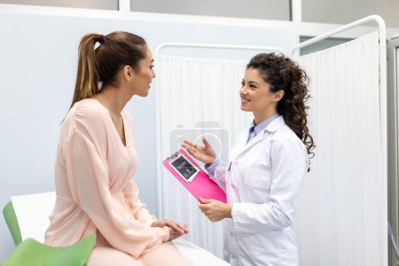 Téléchargez les photos : Gynécologue montrant une photo avec échographie à une jeune patiente, expliquant les caractéristiques de la santé des femmes lors d'une consultation médicale au bureau - en image libre de droit