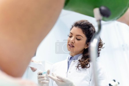 Photo for Experienced female gynecologist in lab coat, holding medical vaginal speculum for examining patient. Young woman lying on gynecological chair during check up. - Royalty Free Image