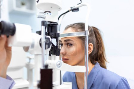 Photo for Attentive optometrist examining female patient on slit lamp in ophthalmology clinic. Young beautiful woman is diagnosed with eye pressure on special ophthalmological equipment. - Royalty Free Image