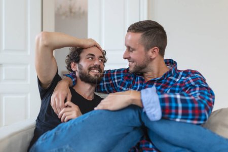 Foto de Ama a la pareja gay masculina del mismo sexo acostada en el sofá en casa y relajándose, abrazándose juntos - Imagen libre de derechos