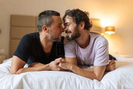 Feliz pareja gay acostada en la cama en casa, abrazándose y coqueteando. LGBT gay pareja amor momentos felicidad concepto