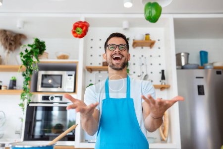 Téléchargez les photos : Joyeux jeune homme jetant des légumes dans l'air à la cuisine - en image libre de droit