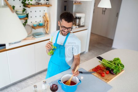 Téléchargez les photos : Heureux homme souriant préparant un repas savoureux. Jeune homme cuisine dans la cuisine. - en image libre de droit