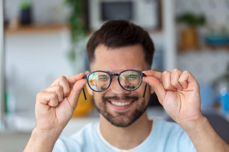 Photo for Young African man holds glasses with diopter lenses and looks through them, the problem of myopia, vision correction - Royalty Free Image