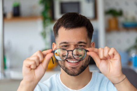 Photo for Young African man holds glasses with diopter lenses and looks through them, the problem of myopia, vision correction - Royalty Free Image