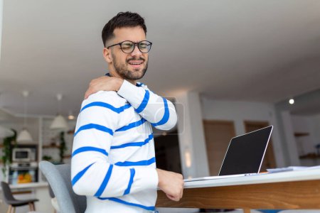 Foto de Joven hombre de negocios horas extras de trabajo y sentir dolor de hombro mientras se utiliza el ordenador portátil en casa - Imagen libre de derechos
