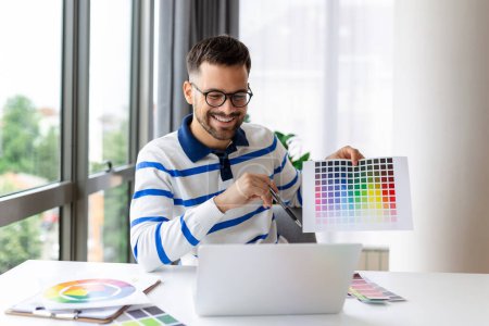 Photo for Young guy showing color swatches at laptop screen at home office, presenting graphic design project on remote meeting. Millennial designer selecting gamma for future house interior - Royalty Free Image