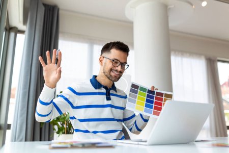 Photo for Graphic Design Courses Online. Young Man Holding Colour Swatch And Using Laptop Computer At Home, Study In Internet, Male Freelance Designer Planning Gamma For Future Interior, Free Space - Royalty Free Image