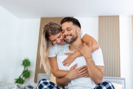 Photo for Portrait of young couple sitting on bed and look at each other. Attractive beautiful new marriage man and woman in pajamas enjoy morning activity in bedroom at home. Family relationship concept. - Royalty Free Image