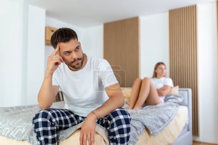 Téléchargez les photos : Beautiful girl and a frustrated man sitting in bed and not looking at each other. Upset couple ignoring each other. Worried man in tension at bed. Young couple angry with each other after a fight. - en image libre de droit