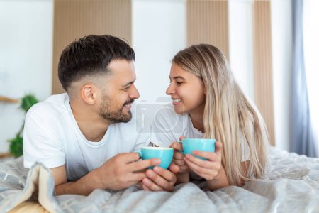 Téléchargez les photos : Jeune couple marié amoureux prenant un café dans leur lit. Bonjour ! Petit déjeuner sain au lit. Jeune beau couple d'amour prend un café au lit. - en image libre de droit