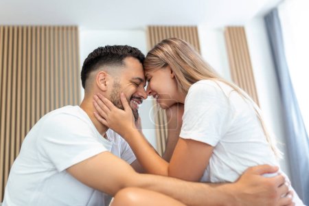 Photo for Affectionate young attractive couple sharing a romantic moment in the bedroom at home. Happy young couple hugging and smiling while lying on the bed in a bedroom at home. - Royalty Free Image
