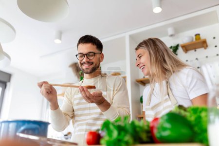 Photo for Portrait of happy young couple cooking together in the kitchen at home. romantic Attractive young woman and handsome man are enjoying spending time together while standing on light modern kitchen. - Royalty Free Image
