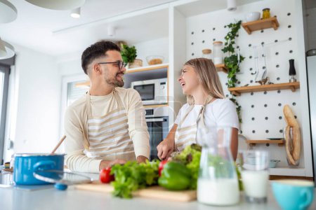 Photo for Smiling young couple cooking food in the kitchen together in the kitchen,having a great time together. Man and woman laughing - Royalty Free Image
