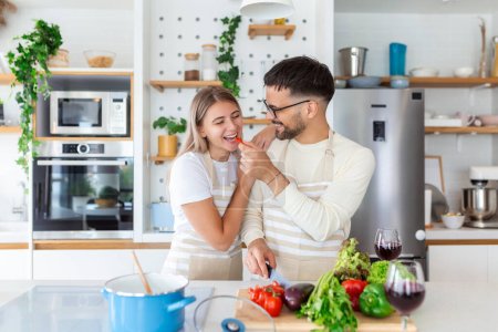 Téléchargez les photos : Portrait de jeunes couples heureux cuisinant ensemble dans la cuisine à la maison. romantique attrayant jeune femme et bel homme aiment passer du temps ensemble tout en se tenant debout sur la cuisine moderne lumière. - en image libre de droit