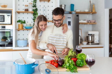 Photo for Portrait of happy young couple cooking together in the kitchen at home. romantic Attractive young woman and handsome man are enjoying spending time together while standing on light modern kitchen. - Royalty Free Image