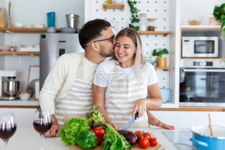 Photo for Happy young couple have fun in modern kitchen indoor while preparing fresh fruits and vegetables food salad. Beautiful young couple talking and smiling while cooking healthy food in kitchen at home. - Royalty Free Image