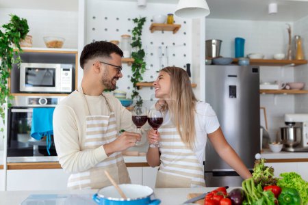 Téléchargez les photos : Couple romantique amoureux passer du temps ensemble dans la cuisine. Mignon jeune couple boire du vin dans la cuisine et profiter du temps ensemble - en image libre de droit