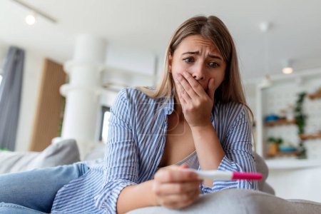 Schockierte Frau blickt auf Kontrolllinie beim Schwangerschaftstest. Eine alleinstehende traurige Frau beschwert sich bei einem Schwangerschaftstest. Depressive Frau mit negativem Schwangerschaftstest.
