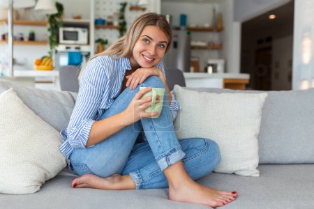 Foto de Retrato de una joven sonriente relajándose sola en su sofá de la sala de estar en casa por la tarde - Imagen libre de derechos