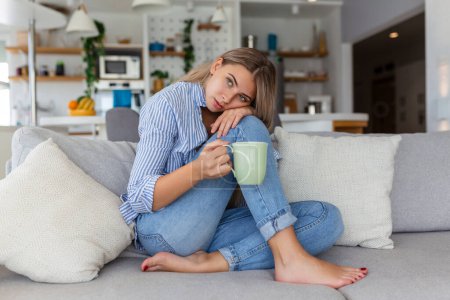 Téléchargez les photos : Portrait d'une jeune femme souriante se relaxant seul sur son canapé de salon à la maison dans l'après-midi - en image libre de droit