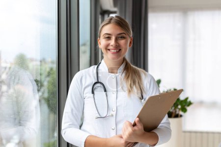 Photo for Confident smiling doctor posing and looking at camera with stethoscope in her hands. Friendly female doctor smiling. Doctor with stethoscope around her neck - Royalty Free Image