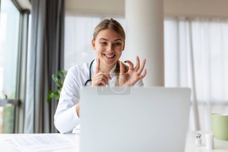 Photo for Attractive female doctor talking while explaining medical treatment to patient through a video call with laptop in the consultation. - Royalty Free Image