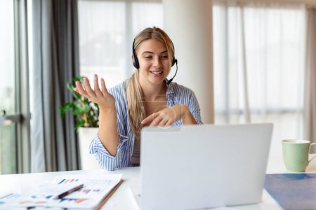 Photo for Happy young woman working on laptop while talking to customer on phone. Consulting corporate client in conversation with customer using computer. Service desk consultant talking in a call center. - Royalty Free Image