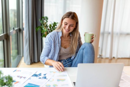 Téléchargez les photos : Concept d'emploi, de technologie et de personnes à distance - jeune femme d'affaires souriante heureuse avec ordinateur portable et papiers travaillant au bureau à domicile - en image libre de droit