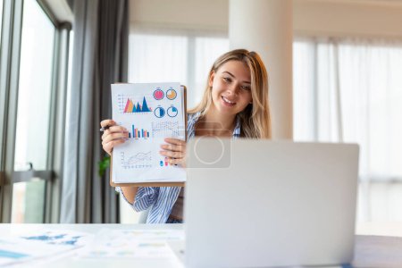 Foto de Focused business woman presenting charts and graphs on video call online. Young business woman having conference call with client on laptop. Young woman explaining how business work - Imagen libre de derechos
