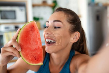 Photo for Young woman eats a slice of watermelon in the kitchen. Portrait of young woman enjoying a watermelon. - Royalty Free Image