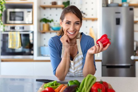 Nette, fröhliche, brünette Frau in guter Laune bereitet in der Küche ihres Hauses einen frischen veganen Salat für ein gesundes Leben zu.