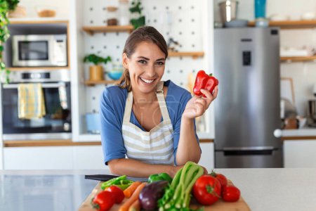 Foto de Linda joven morena feliz de buen humor preparando una ensalada vegana fresca para una vida saludable en la cocina de su casa. - Imagen libre de derechos
