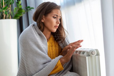 Photo for Unwell woman renter in blanket sit in cold living room hand on old radiator.suffer from lack of heat . Unhealthy young woman struggle from chill freeze at home. No heating concept. - Royalty Free Image