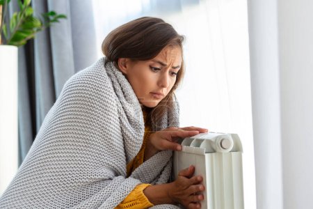 Téléchargez les photos : Femme gelée à la maison, assise près du radiateur froid. Femme avec problème de chauffage à la maison sensation de froid - en image libre de droit