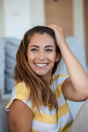 Photo for Happy young woman sitting on sofa at home and looking at camera. Portrait of beautiful woman smiling and relaxing during summer. - Royalty Free Image