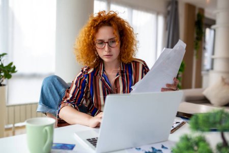 Téléchargez les photos : Femme d'affaires concentrée utilisant un ordinateur portable à la maison, regardant l'écran, bavardant, lisant ou écrivant un courriel, assise sur le canapé, étudiante faisant ses devoirs, travaillant sur un projet de recherche en ligne - en image libre de droit