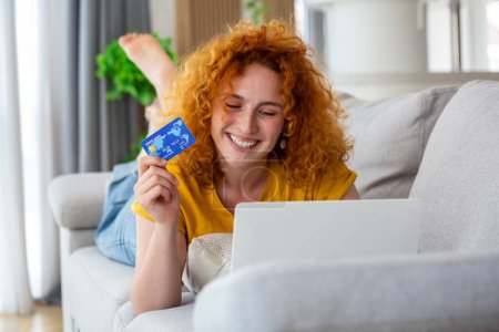 Foto de Female consumer spending buying on internet, lifestyle. Happy woman shopping online with laptop at home. Woman using laptop computer shopping on line, using credit card playing online, smiling indoors - Imagen libre de derechos