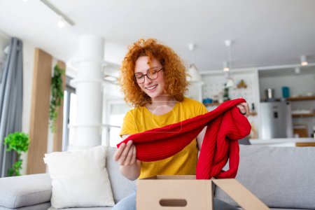 Photo for Young woman receiving parcel at home. Holiday shopping online and unpacking cardboard box. Delivery service during covid quarantine. Happy girl getting gift. Lifestyle moment - Royalty Free Image